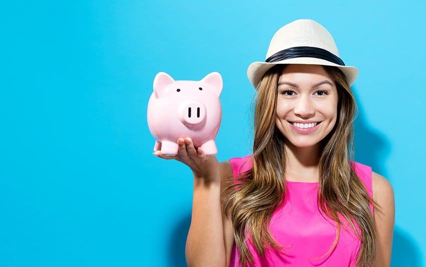 Young woman with a piggy bank on a blue background showing off her affordable cosmetic dental treatment.