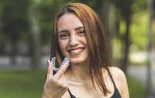 attractive young woman preparing to place her Invisalign clear aligners in her mouth