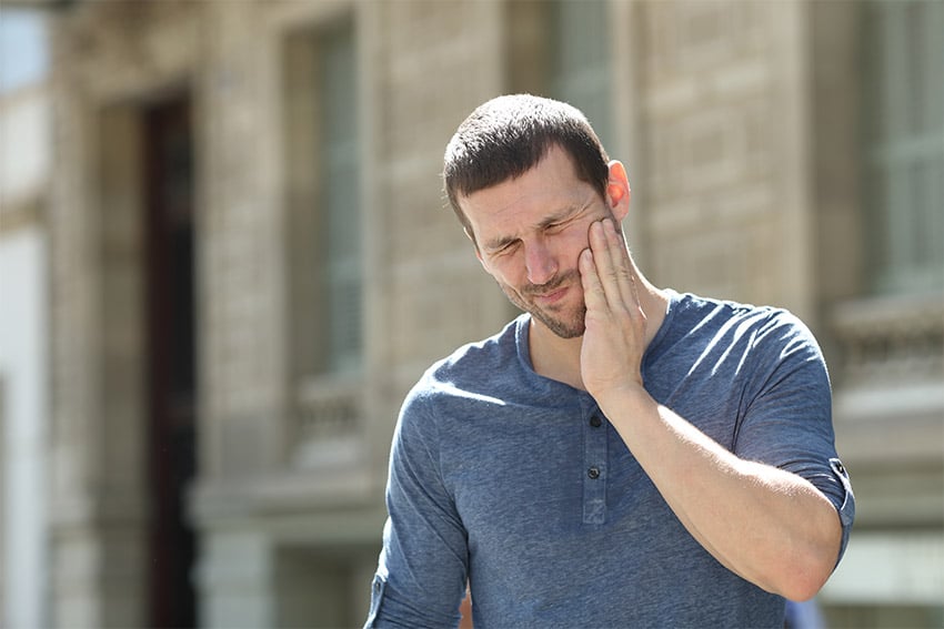 man walking on the street holds the side of his face due to pain