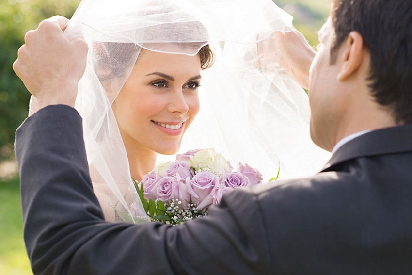 blushing bride having her veil lifted by groom