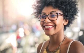 woman with curly hair and glasses shows off her white smile