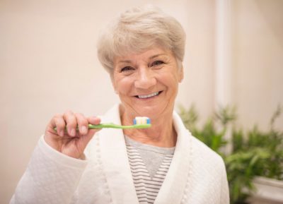 woman brushing her teeth, taking care of her dental implants