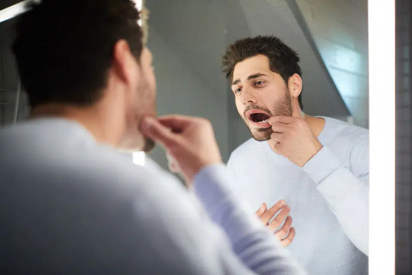 young adult man looking at this mouth in the mirror