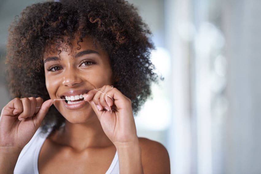 adult woman smiling and flossing her white teeth