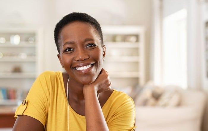 Woman with short hair in yellow shirt leaning head on hand and smiling